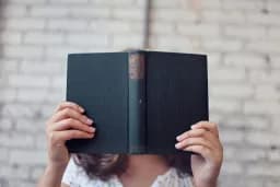 Persona leyendo un libro de tapas oscuras que le tapa la cara